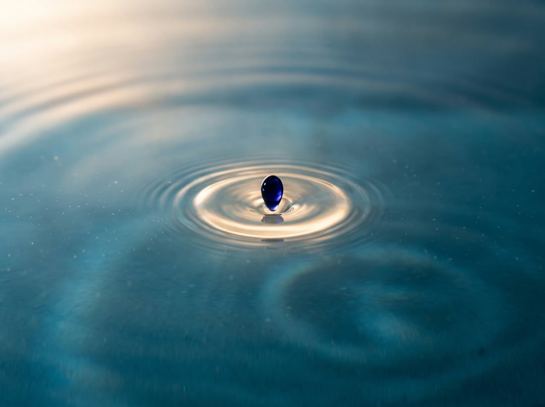 Ein einzelner Tintentropfen trifft die Wasseroberfläche und zieht erste Ringe